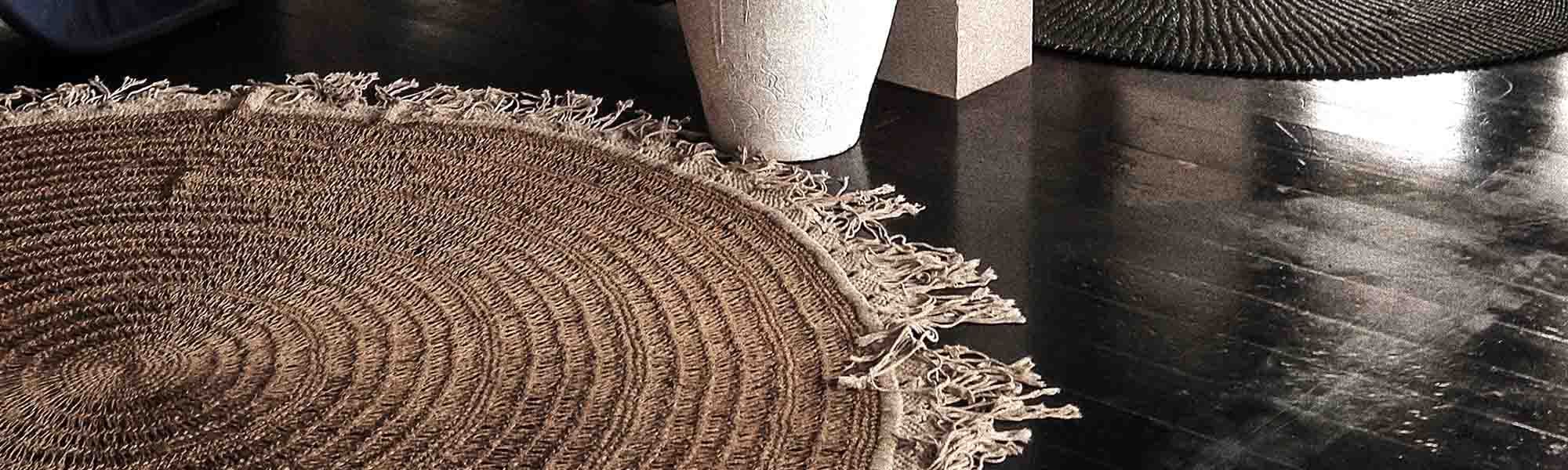 A woven round door mat on a black wooden floor