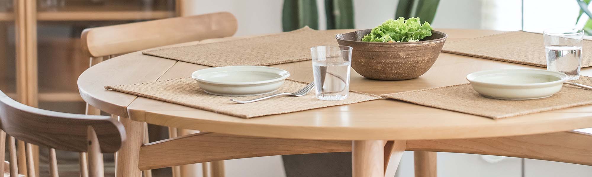 A round wooden dining table is served with dishes and chairs around it