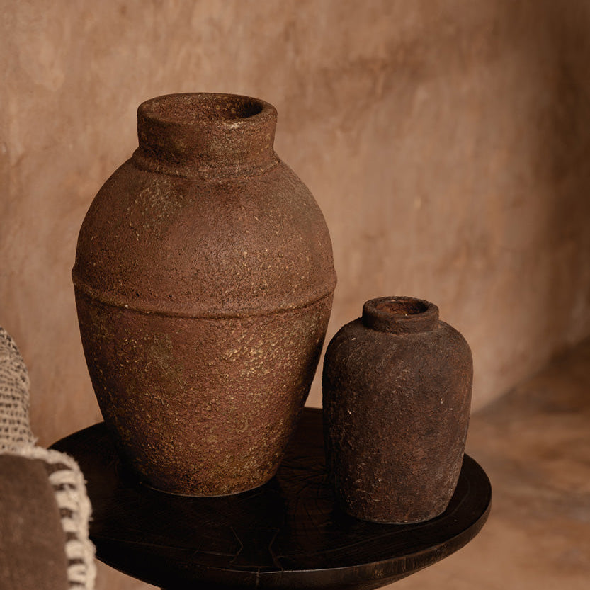 Two brown pots on a dark pedestal against a beige wall.