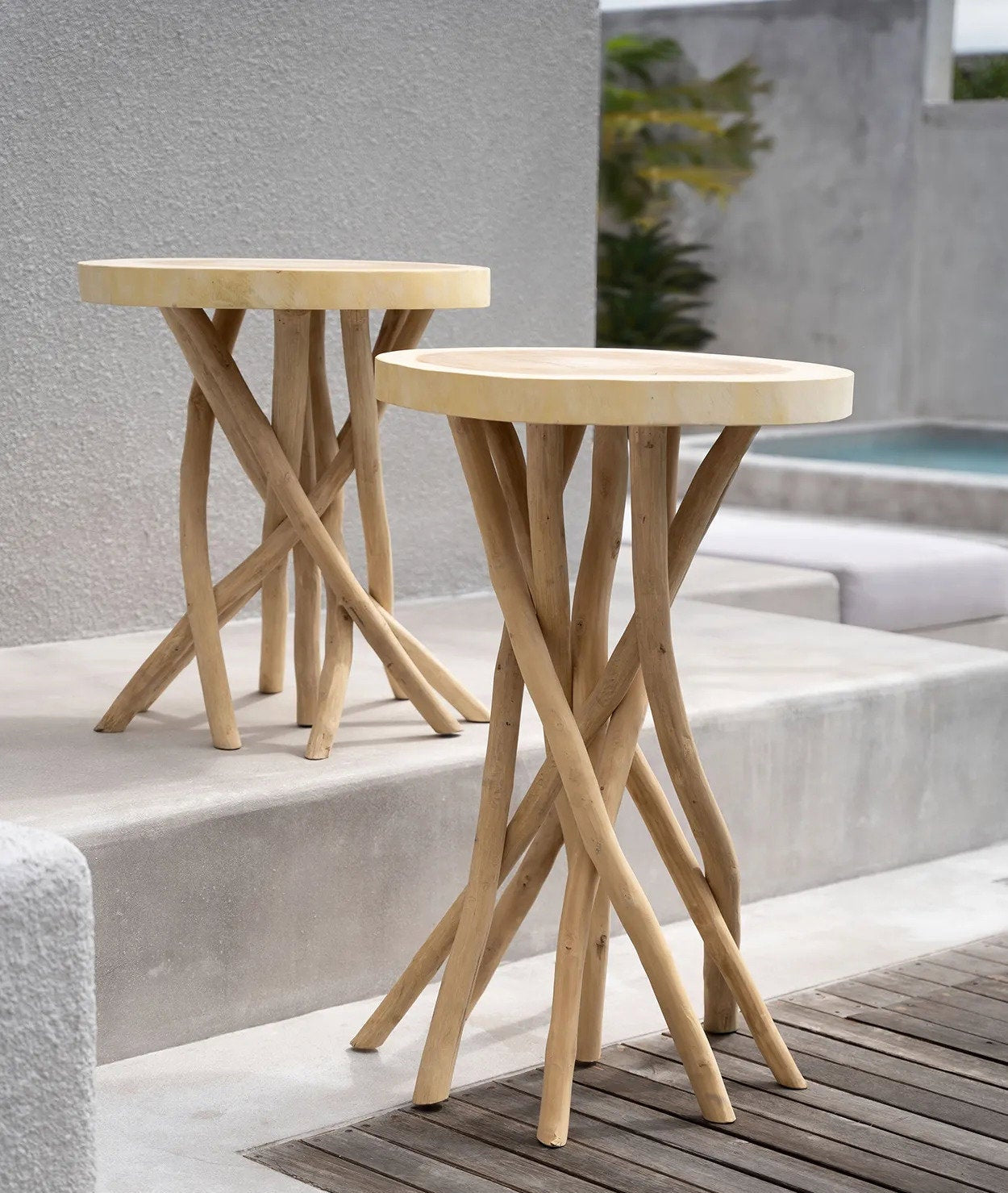 Two wooden side tables on a concrete surface with a pool in the background