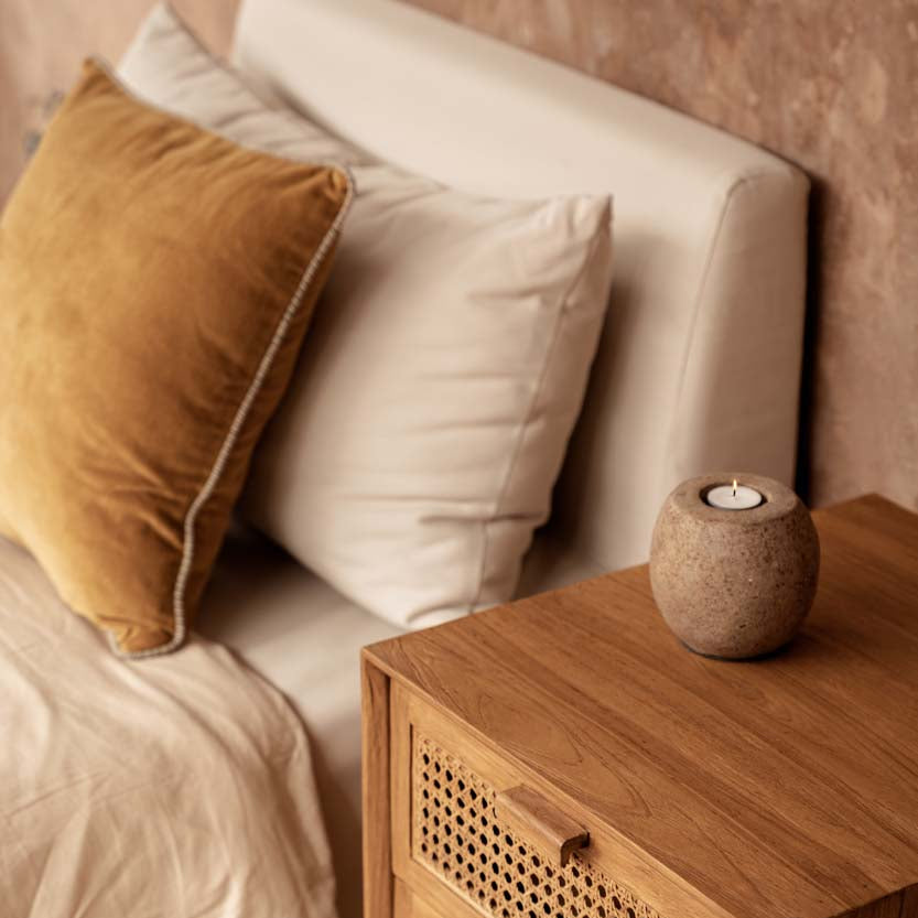 Wooden nightstand with candle holder next to a bed with pillows