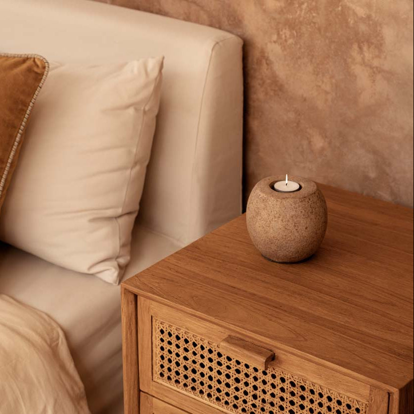Bed with beige pillows and a wooden nightstand with a candle.