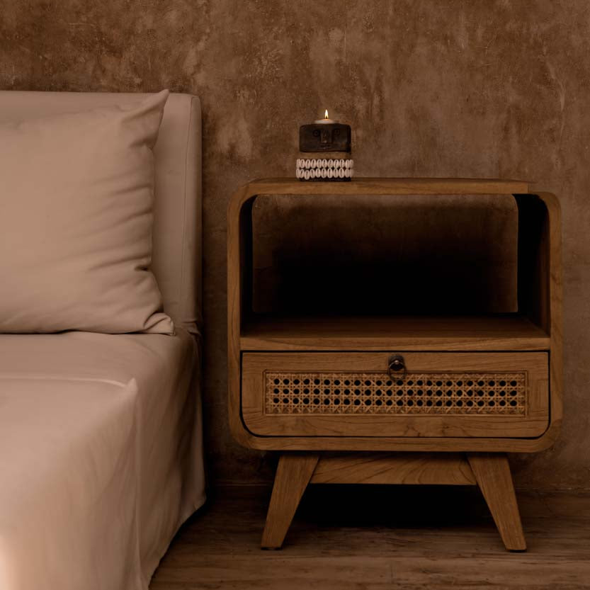 Wooden nightstand next to a bed with beige bedding in a bedroom setting.