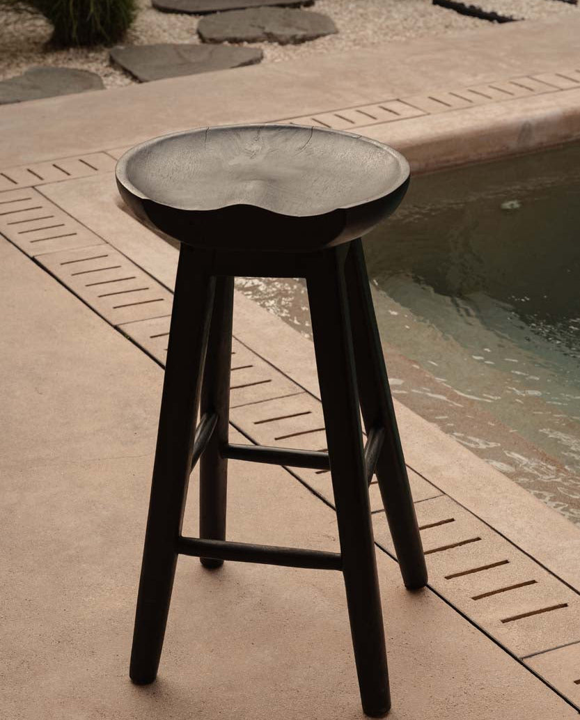 Black bar stool with a round seat on a patio near a pool