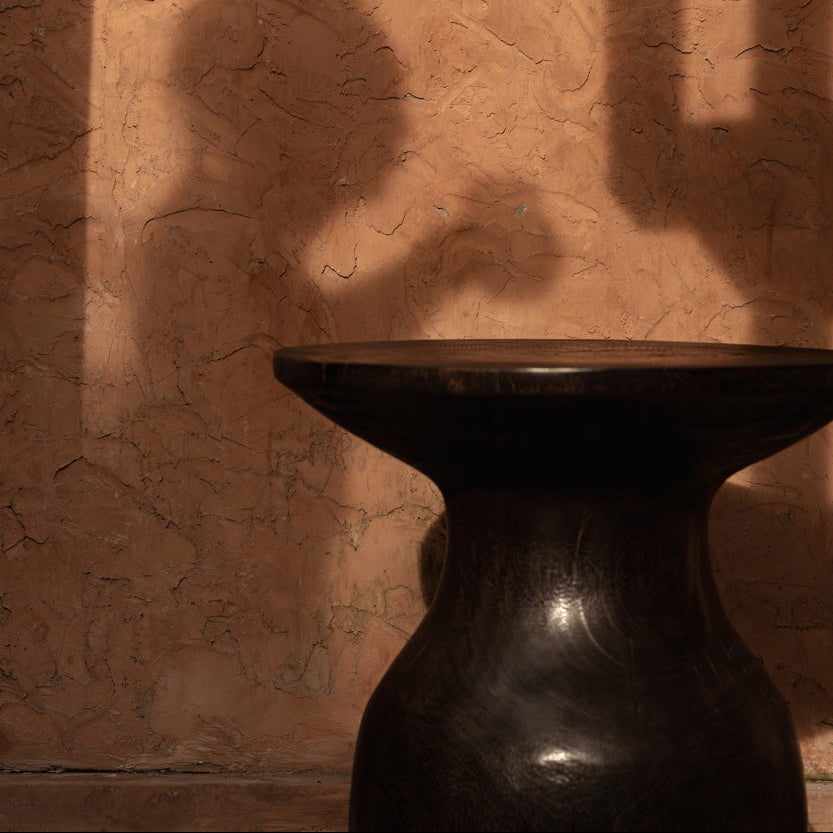 Dark walnut side table against a textured wall with shadows