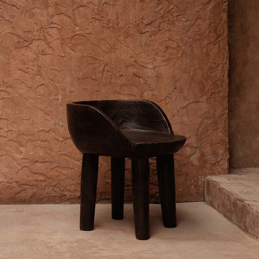 Dark walnut wooden low chair against a textured brown wall.