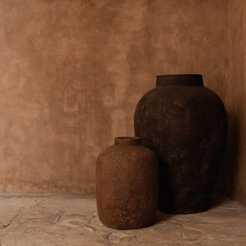 Two rustic vases against a textured wall with a woven basket.