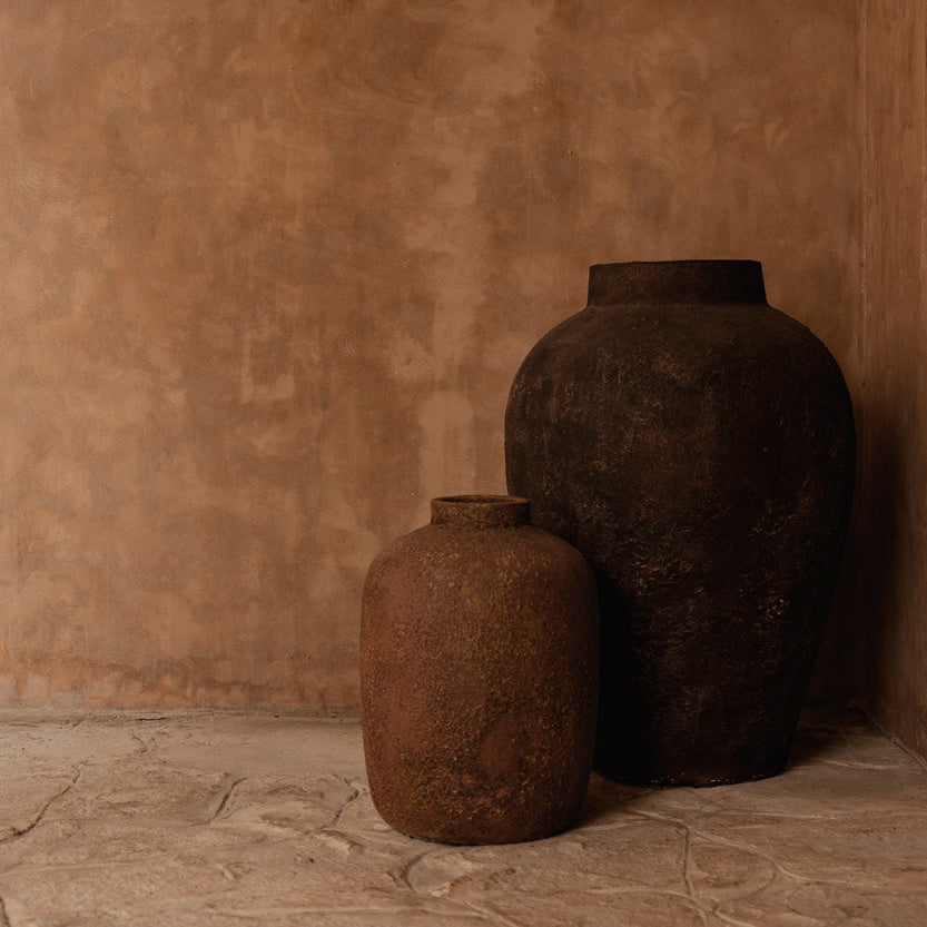 Two rustic terracotta vases against a brown wall 