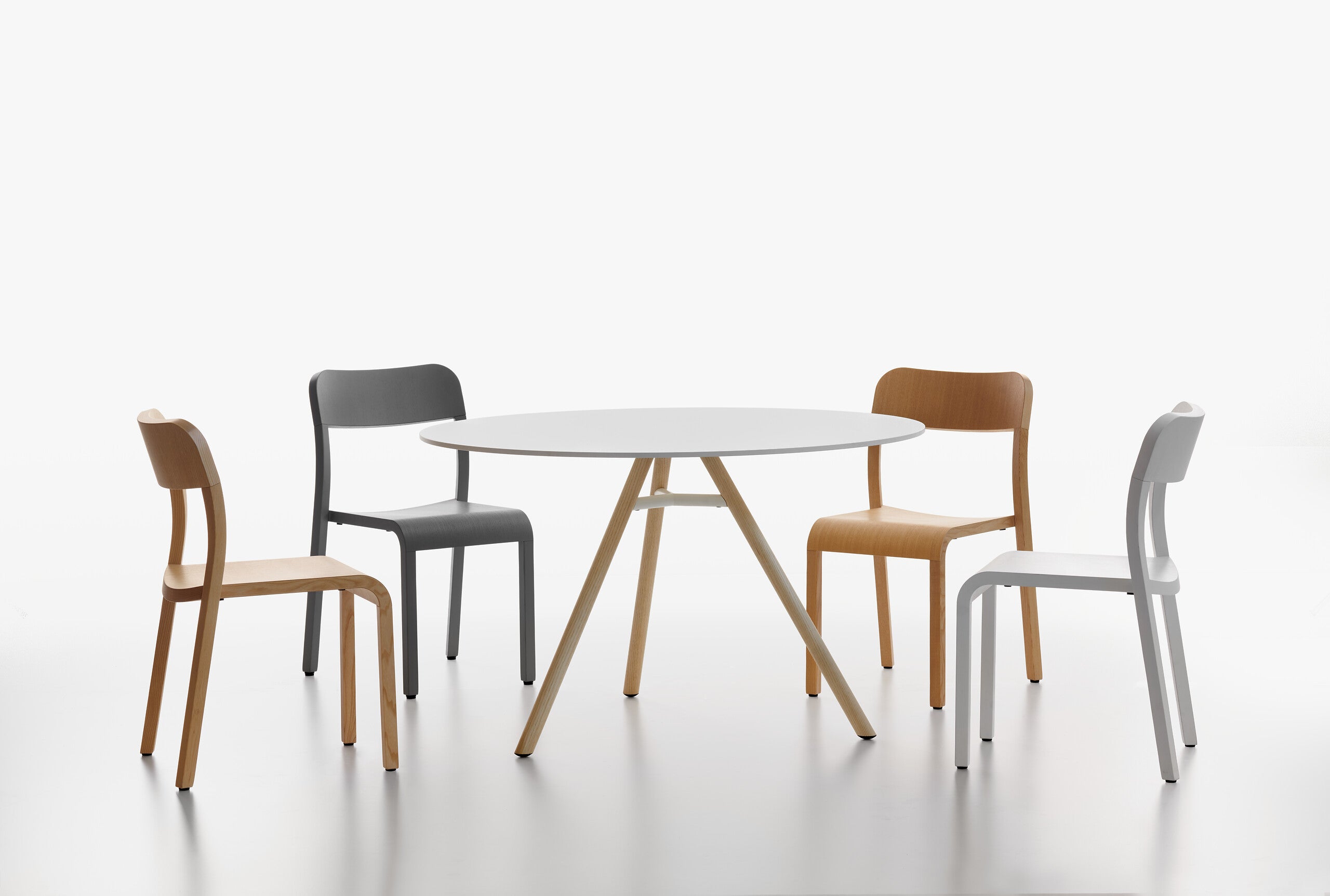 A minimalist dining set featuring a round white MART table, surrounded by four chairs in different colours, set against a seamless white studio background.