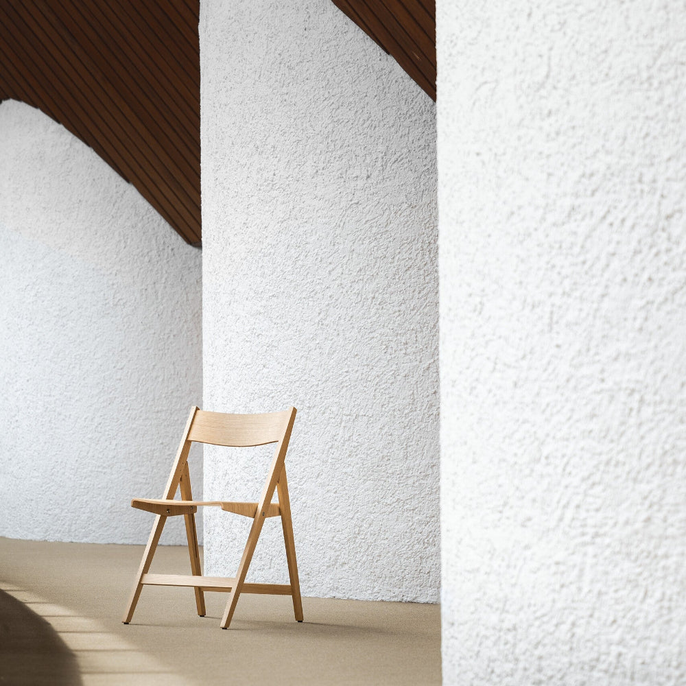 THEO wooden chair against a textured white wall with a wooden ceiling.